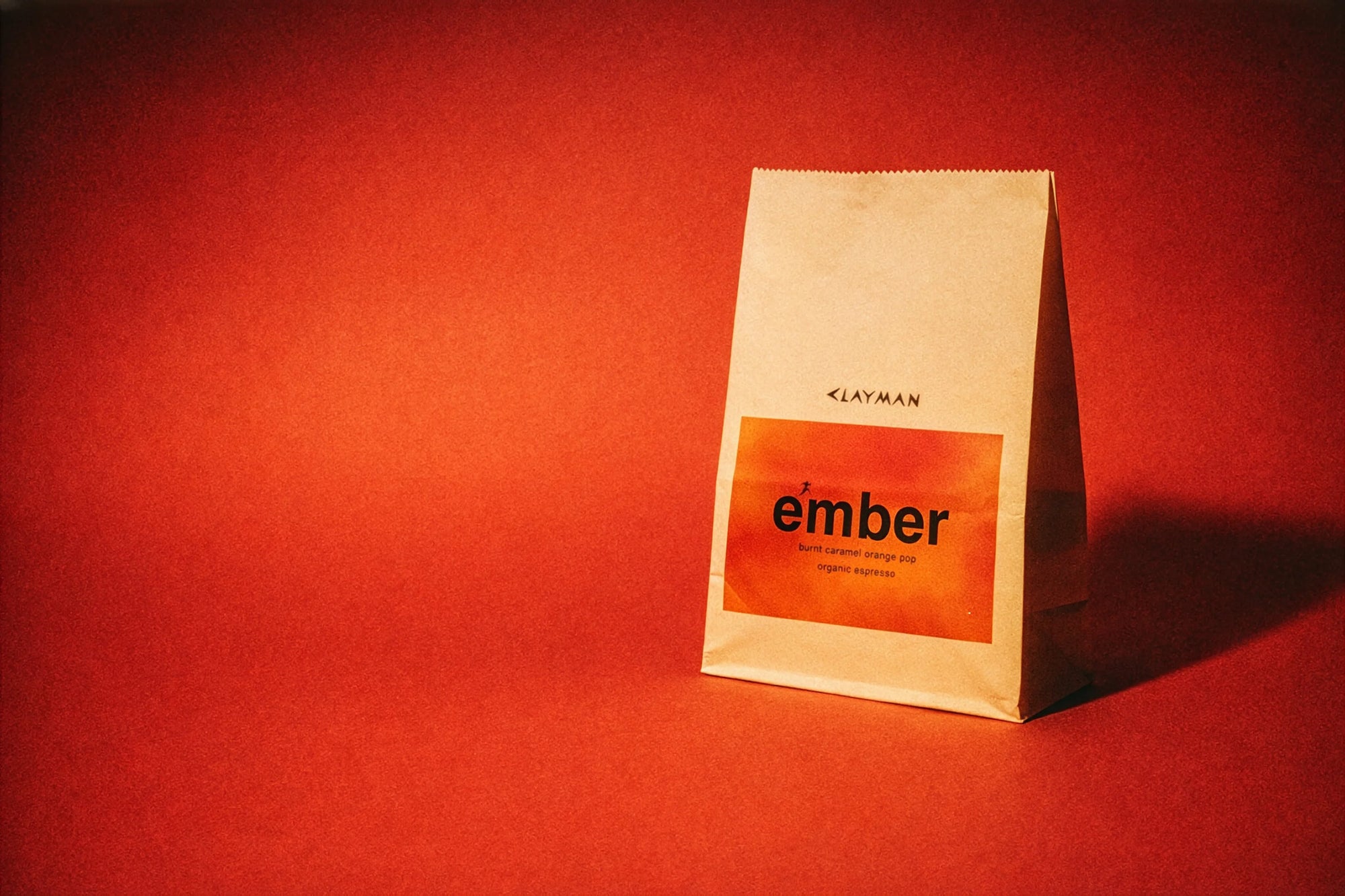 clayman coffee organic coffee beans on red background hero image. Organic ember blend in paper coffee bean bag.